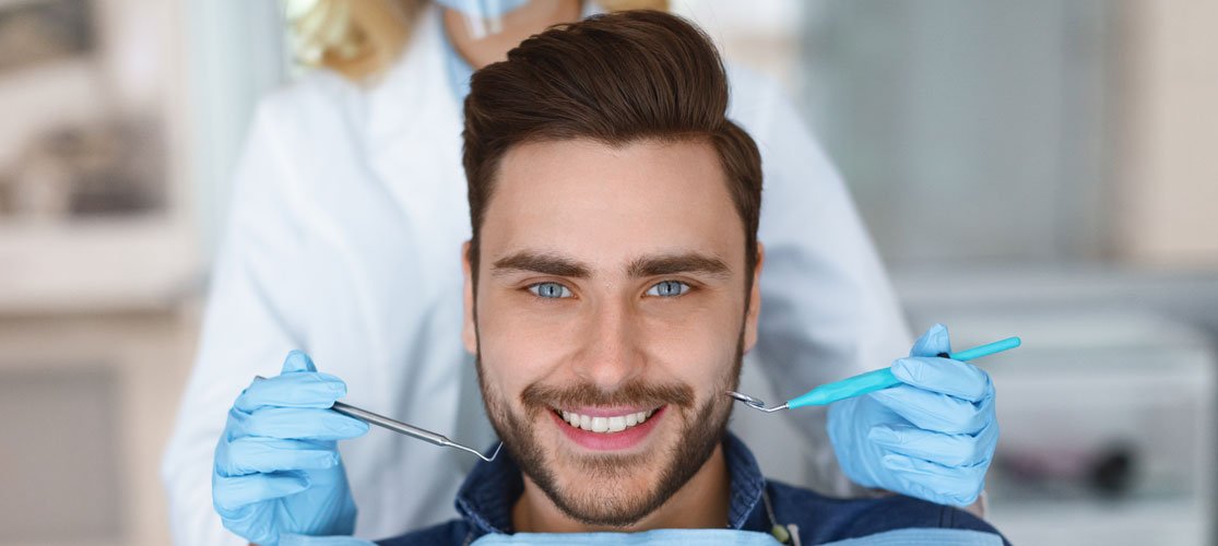 Dental Checkups for Adults Smiling adult patient with a dentist holding examination instruments beside his mouth