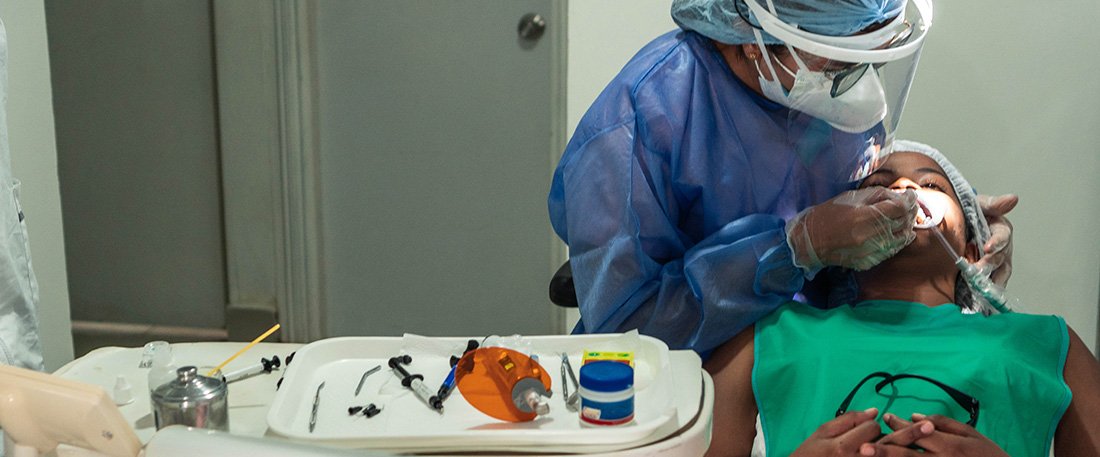 Dental professional wearing a face shield treating a patient in a dental chair