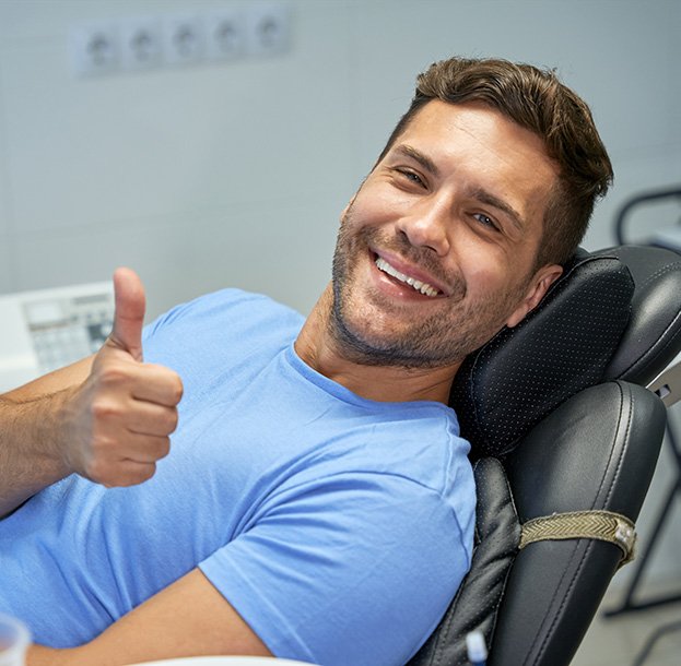 Smiling patient giving a thumbs-up while reclining in a dental chair