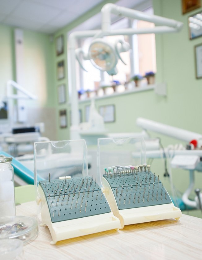 Dental instrument holders on a counter with a treatment chair and overhead light behind them